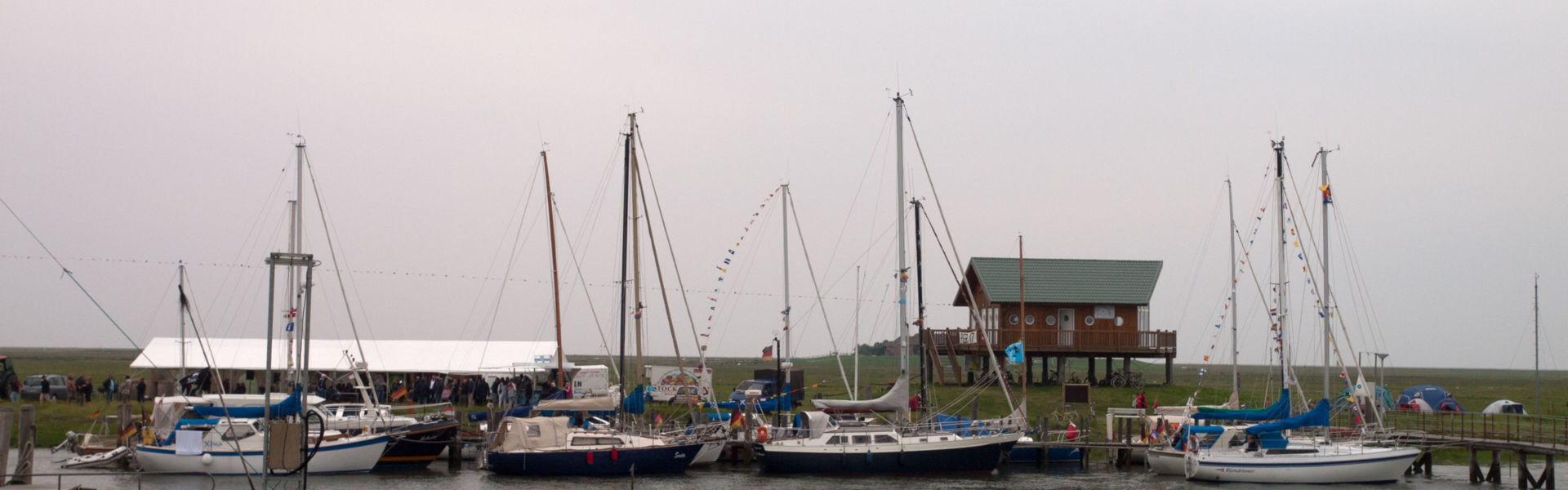 Schleusenfest auf Hooge, Segelboote liegen im Hafen, dahinter ein Festzelt